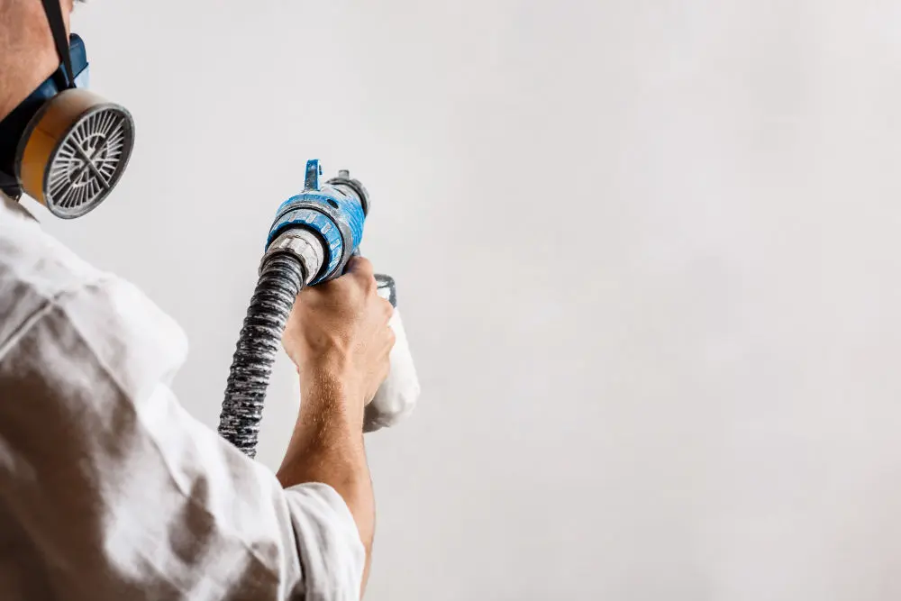 Worker painting wall with spray gun Masonry Cream